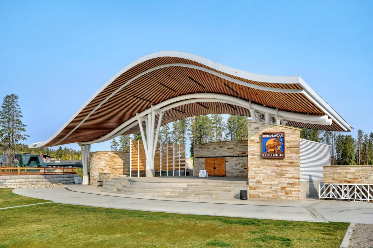 This image showcases a striking outdoor amphitheater with a curved roof structure, stone walls, and wooden beams. The open-air venue is ideal for seasonal events, concerts, and community gatherings.