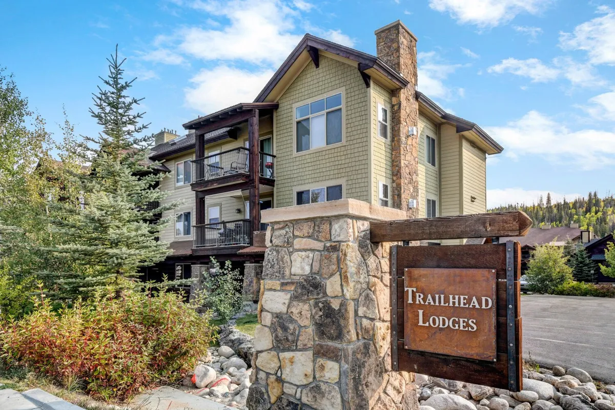 This exterior image showcases the welcoming stone entrance of Trailhead Lodges, highlighted by a prominent sign, rustic balconies, and lush surrounding greenery. The scene hints at the property’s blend of private comfort and nature-connected leisure, capturing the first impression of an upscale, resort-style community.
