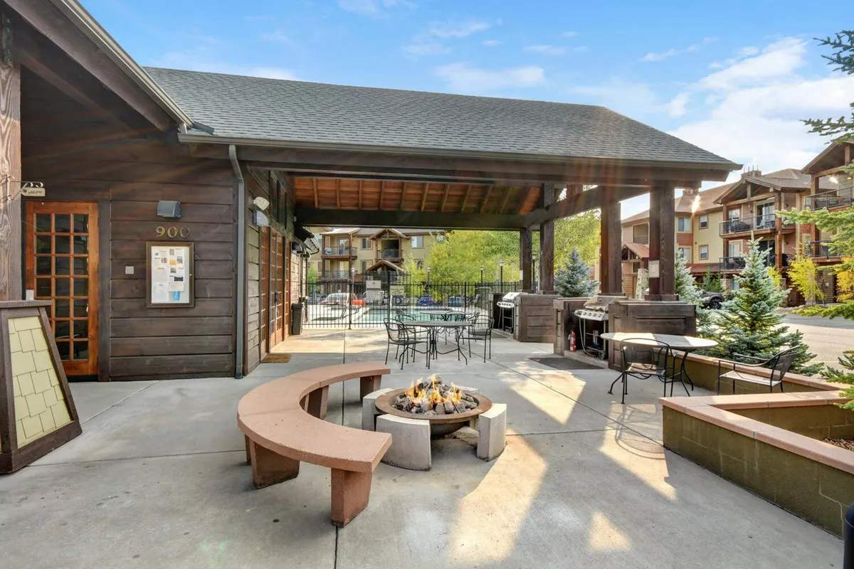 An inviting outdoor scene featuring a cozy fire pit, ample seating, a barbecue grill, and mature trees. This communal area is designed for relaxing evenings, socializing with friends, and enjoying the tranquil natural surroundings—embodying the spirit of resort-style amenities and leisurely outdoor living.
