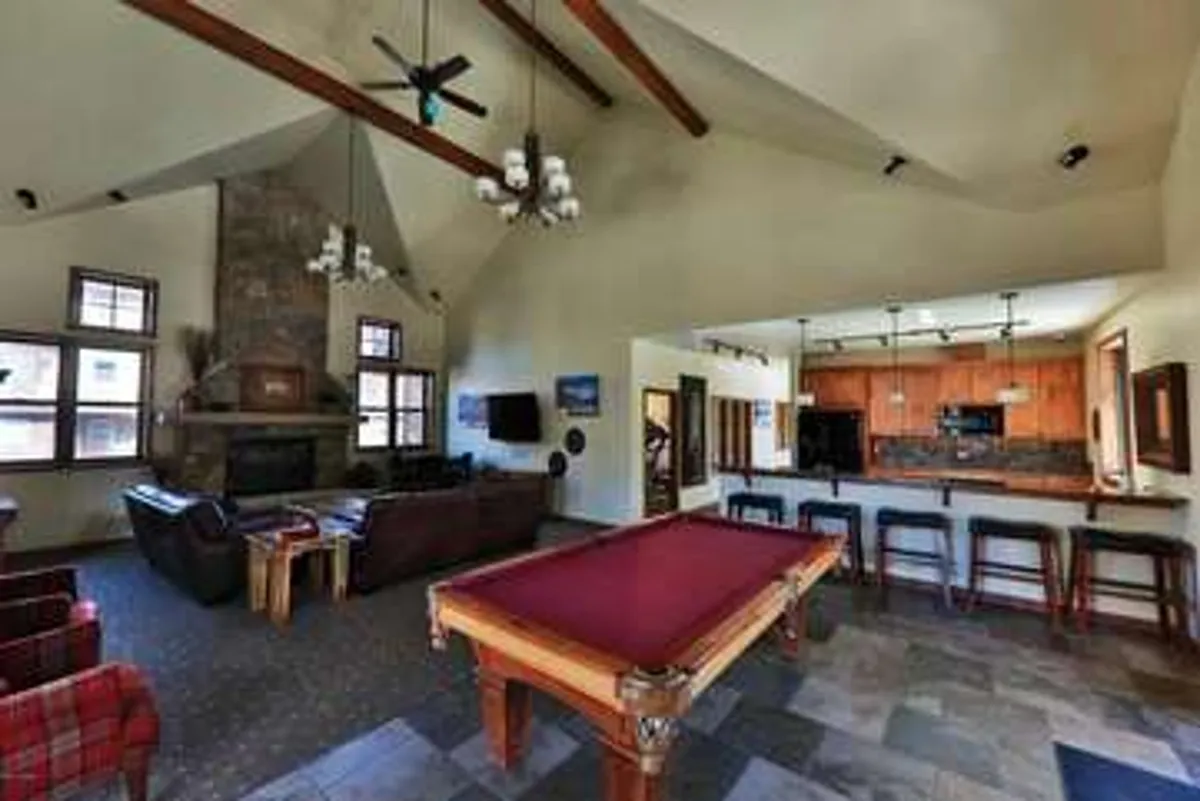 An inviting clubhouse interior featuring a pool table for game nights, a cozy fireplace, ample sofa seating for socializing, and a spacious kitchen bar—perfect for entertaining or relaxing with friends. The space is designed for comfort and versatility, allowing residents to gather for games, casual meals, or holiday celebrations.