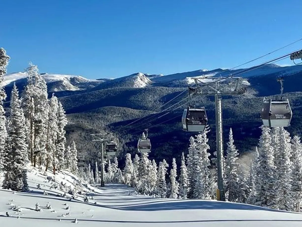 A panoramic view of ski lifts ascending snowy slopes, surrounded by snow-covered pines and rugged mountain peaks under a sunrise sky. The shot exudes anticipation for adventure and the majestic beauty of the Winter Park area.
